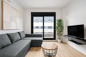 A modern living room with a grey sectional sofa, a round coffee table, a potted plant, and a flat-screen TV mounted on the wall.