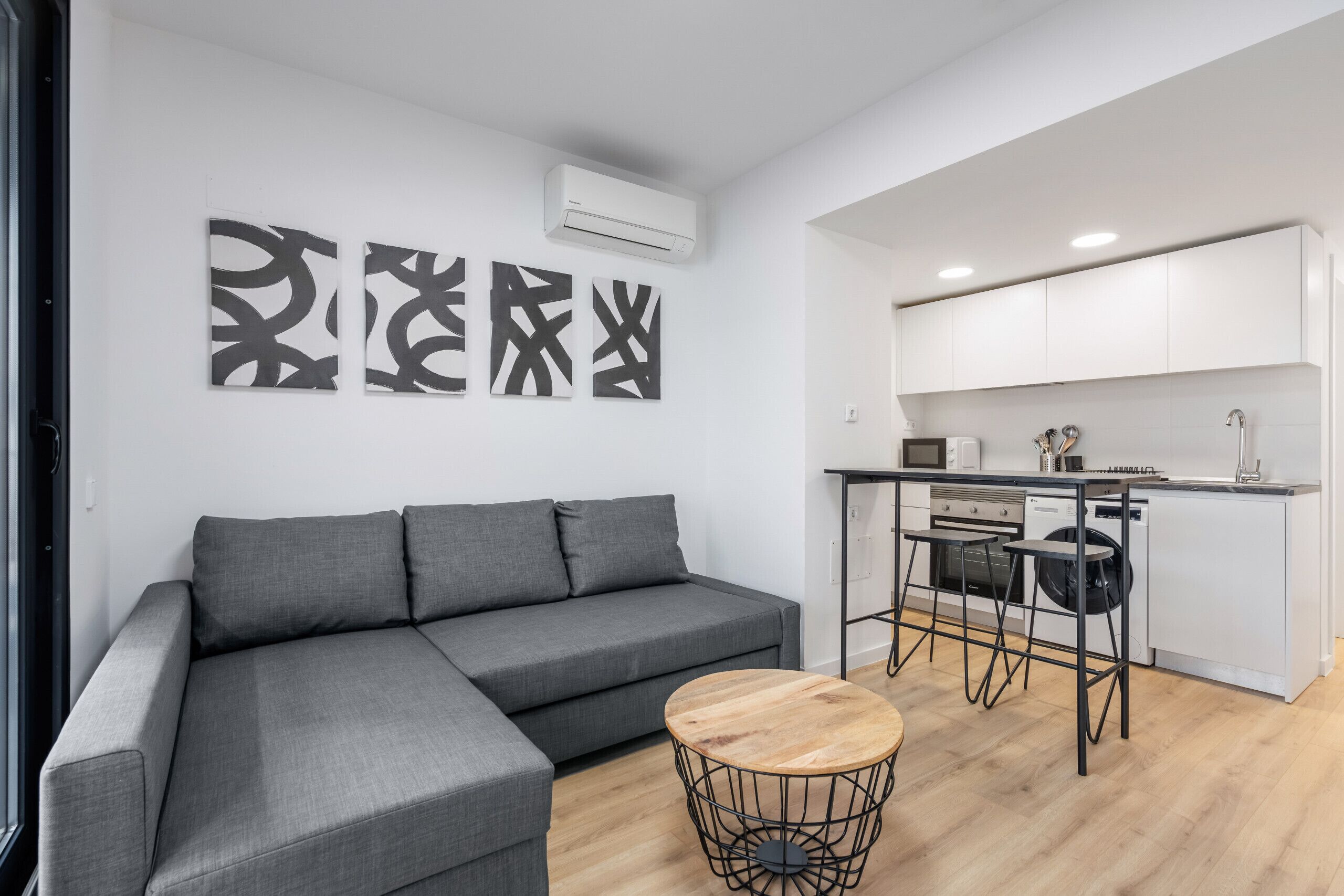 Una sala de estar moderna con un sofá seccional gris, una mesa de centro redonda de madera y arte abstracto en la pared.