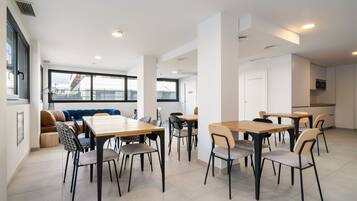 Un'area pranzo moderna con diversi tavoli e sedie, un divano e un'ampia finestra vista edificio.