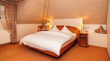 Ein Schlafzimmer mit Holzboden, einem Bett mit weißer Bettwäsche, zwei Nachttischen mit Lampen und einem gemusterten Vorhang.