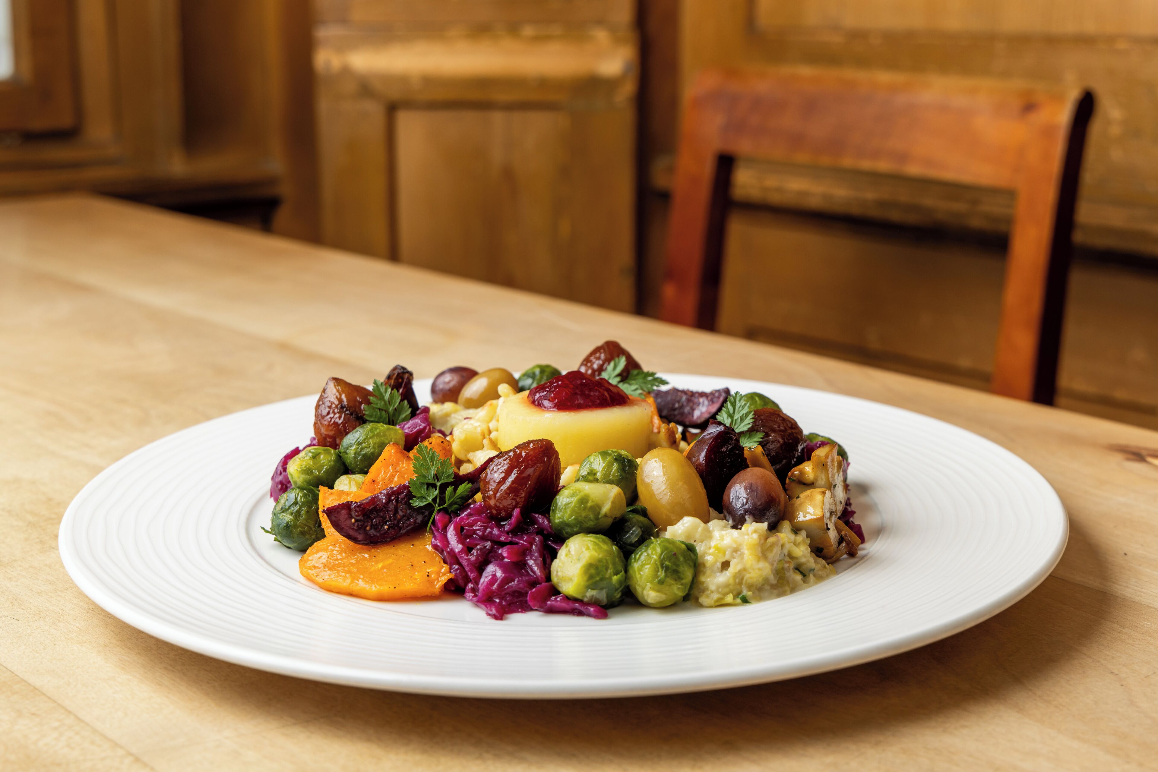 Une assiette blanche contenant une variété de légumes et un morceau de viande, posée sur une table en bois.