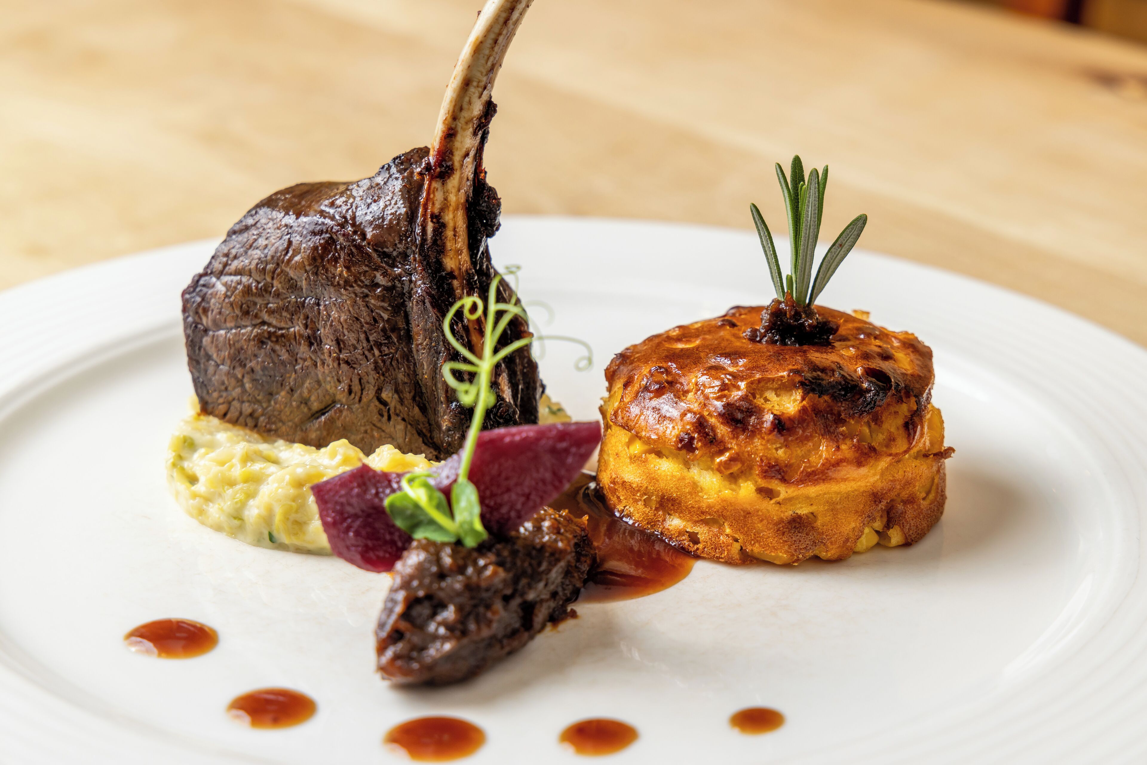 A plate with a lamb shank, a baked item, and some garnishes.