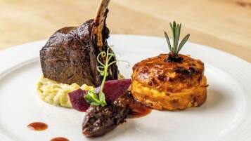 A plate with a lamb shank, a baked item, and some garnishes.