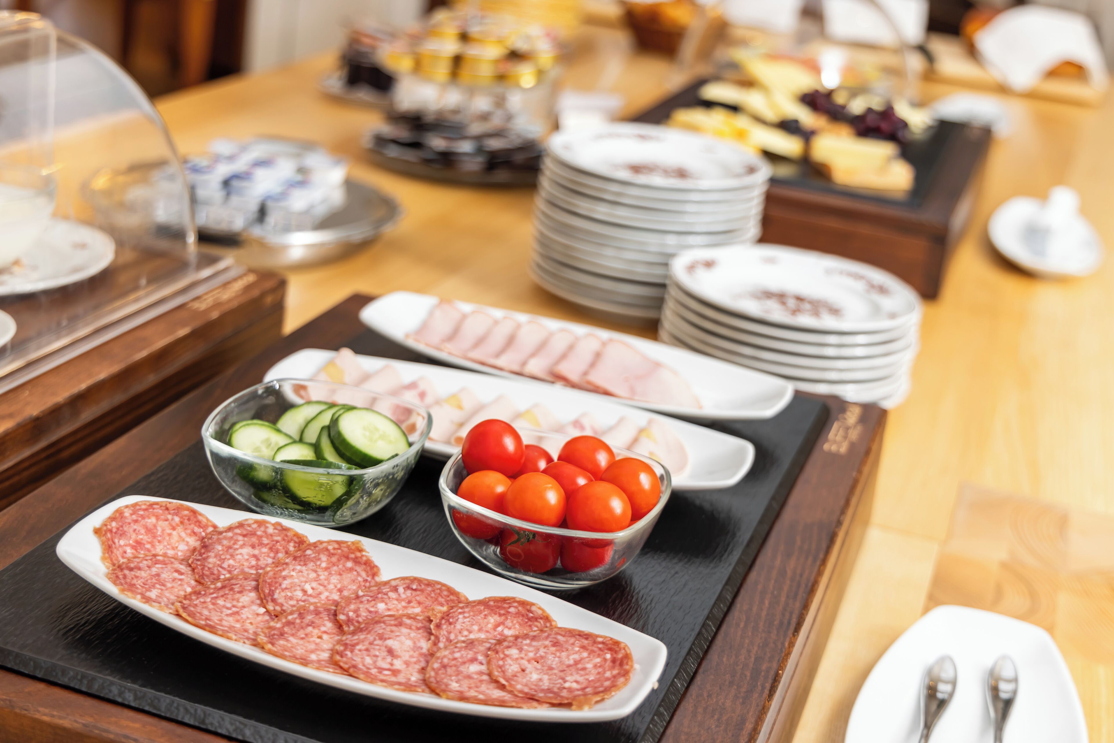Una mesa de buffet con diferentes opciones de comida, incluyendo carnes en rodajas, pepinos y tomates cherry.