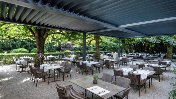 Un área de comedor al aire libre con mesas y sillas, rodeada de árboles y vegetación.