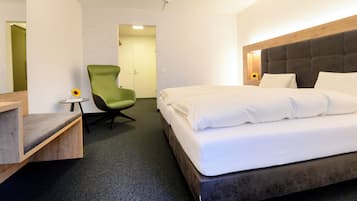 Ett hotellrum med en säng, en grön stol, ett litet bord och en dörr som leder till ett annat rum.