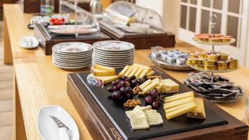 A buffet with various cheeses, fruits, and desserts.