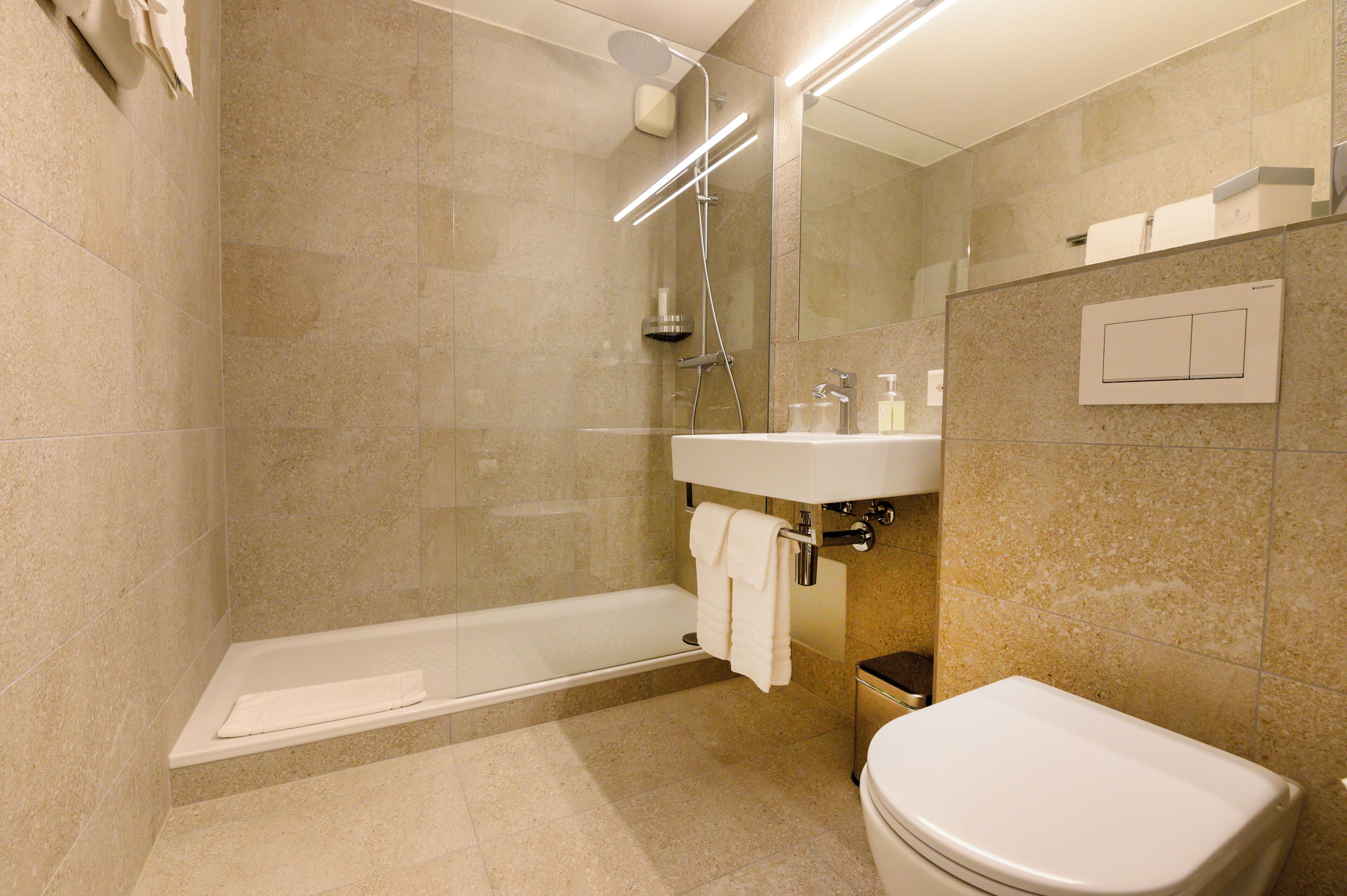 Un baño moderno con ducha de vidrio, un lavabo blanco y un inodoro.