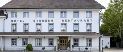 A white building with "HOTEL STERNEN RESTAURANT" signage, multiple windows, and potted plants.