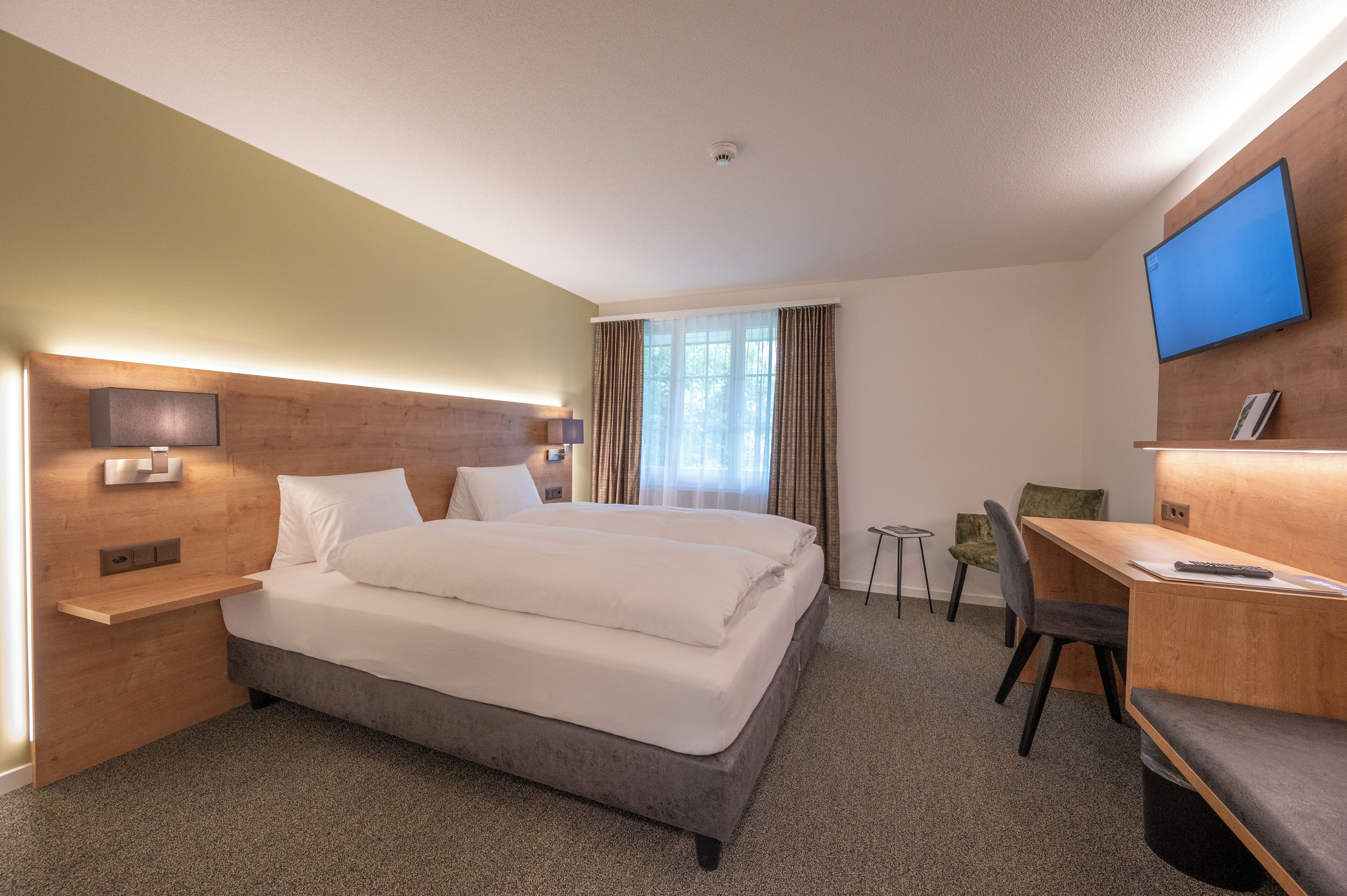 A hotel room with a large bed, a desk, a chair, a TV, and a small table.