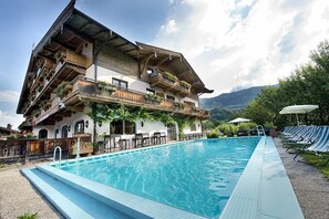 A traditional Alpine-style building with a swimming pool, outdoor seating, and mountain views. - Hotel Alpenhof (Aurach bei Kitzbuehel)