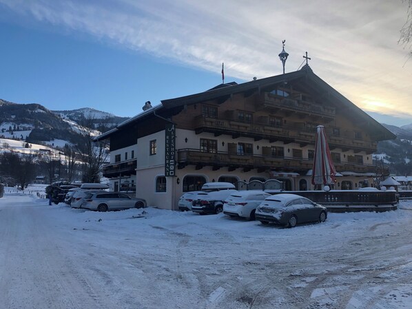 Un hôtel avec une enseigne indiquant « Restaurant Alpenhof », situé dans un paysage enneigé avec des montagnes en arrière-plan.
