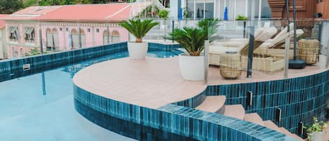 A rooftop pool with a curved edge, lounge chairs, and potted plants.