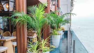 Un balcón con plantas en macetas, muebles de madera y vistas al mar.