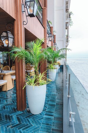 A balcony with potted plants, wooden furniture, and a view of the sea. - Hotel Río Guayas by Art Hotels Ecuador   (Guayaquil)