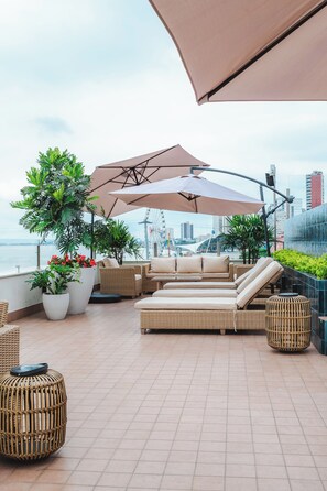 Un salón en la azotea con asientos al aire libre, plantas en macetas y vistas del horizonte urbano.