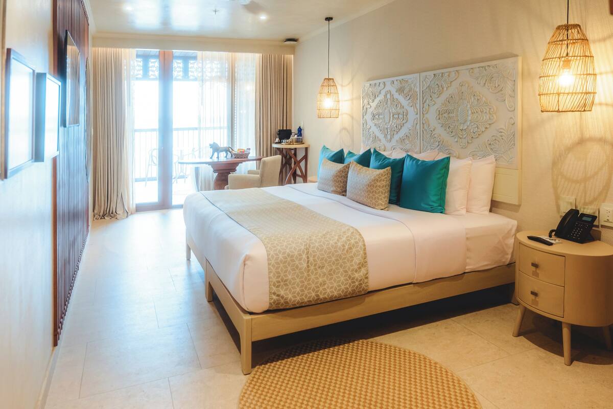 A hotel room with a large bed, bedside tables, a small desk, and a view of the outside.
