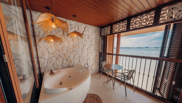 A bathroom with a bathtub, a stone wall, a window with a view, and a table with chairs. - Hotel Río Guayas by Art Hotels Ecuador   (Guayaquil)
