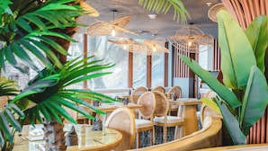A restaurant with round tables, wicker chairs, and large green plants. - Hotel Río Guayas by Art Hotels Ecuador   (Guayaquil)