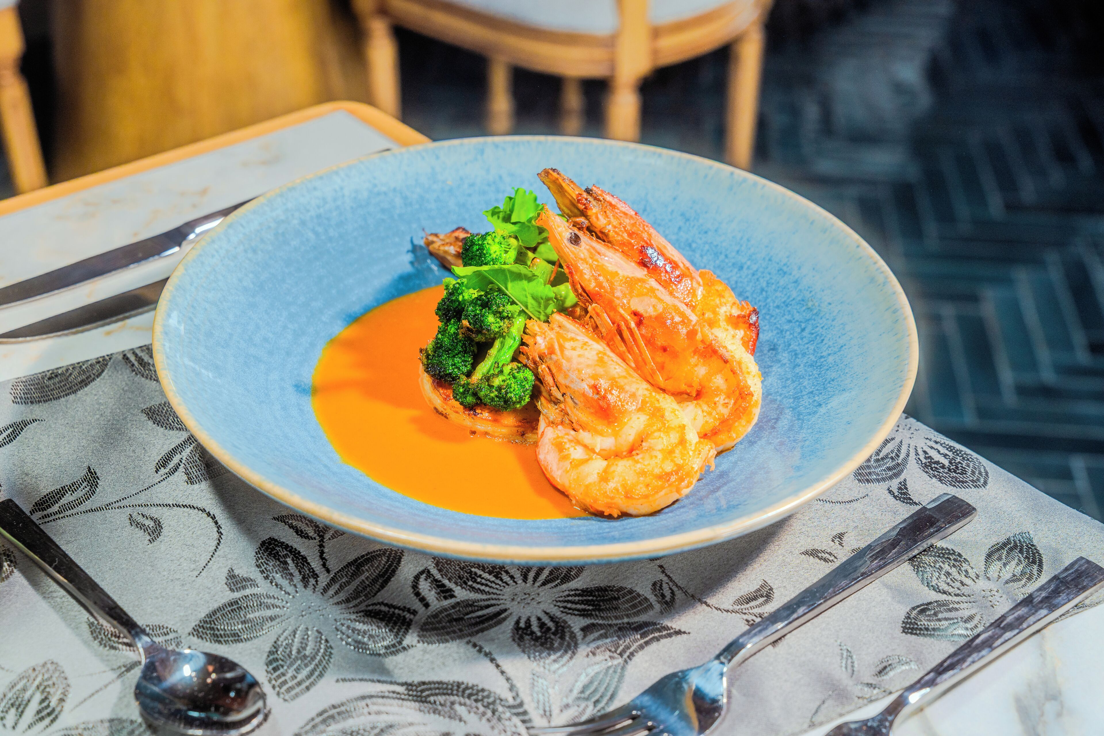 A plate of food with shrimp and broccoli on a table with a patterned tablecloth.