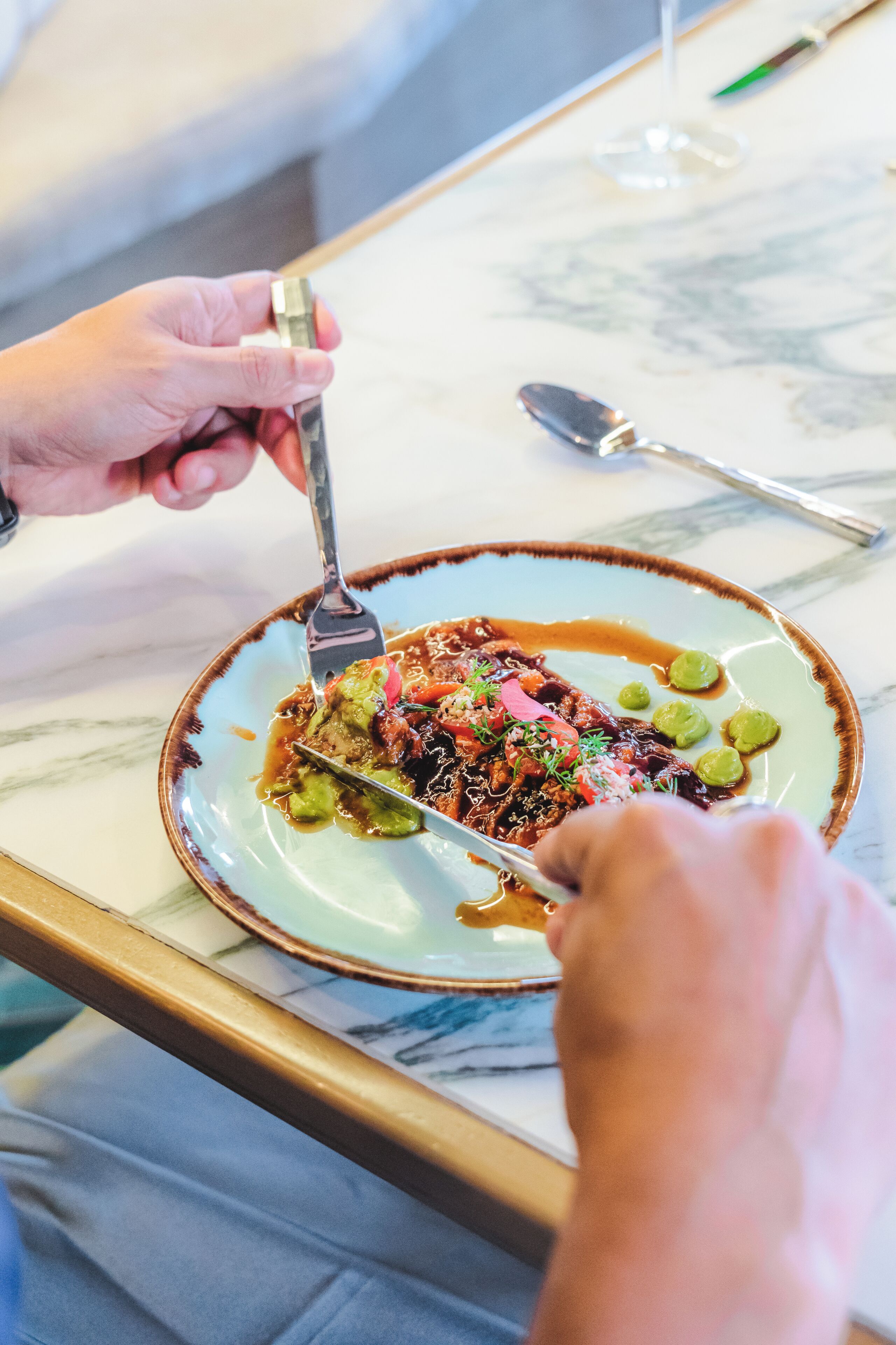 A person dining at a table with a plate of food, a spoon, and a fork.