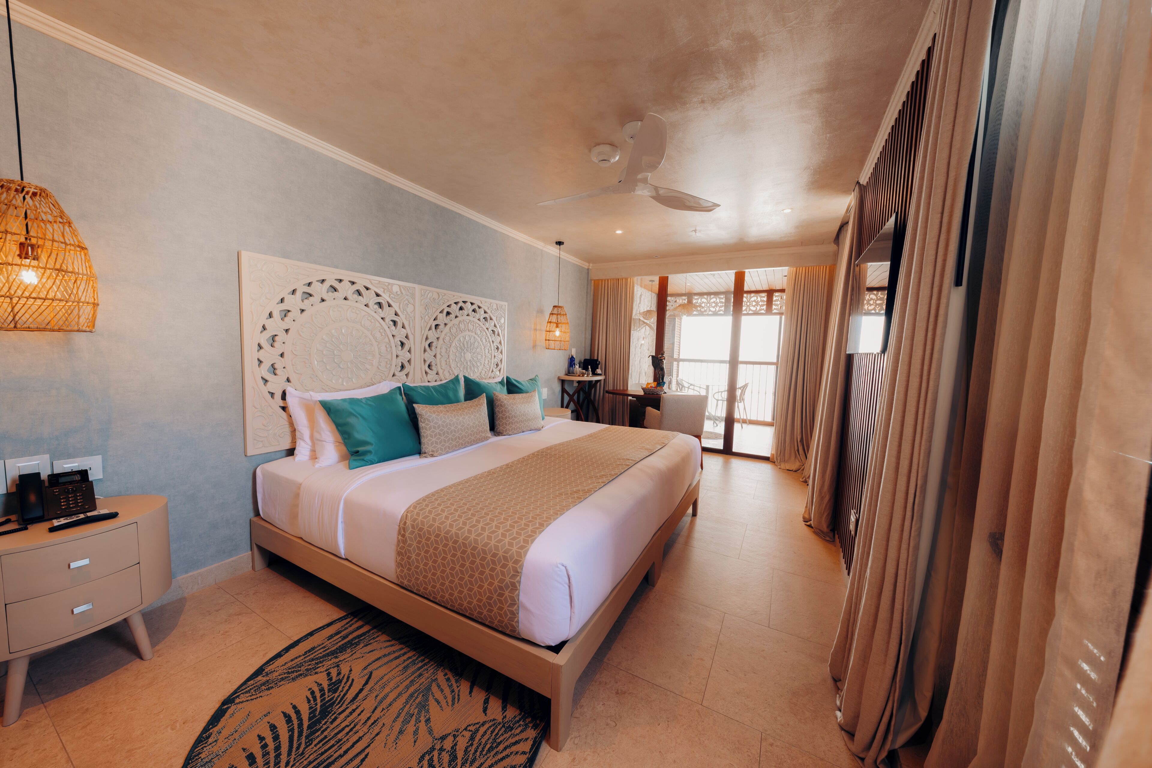 A spacious bedroom with a large bed, a ceiling fan, a nightstand, and a view of the outside through a window.
