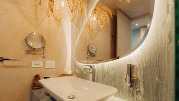 Un baño con lavamanos blanco, un espejo grande e iluminación de mimbre.