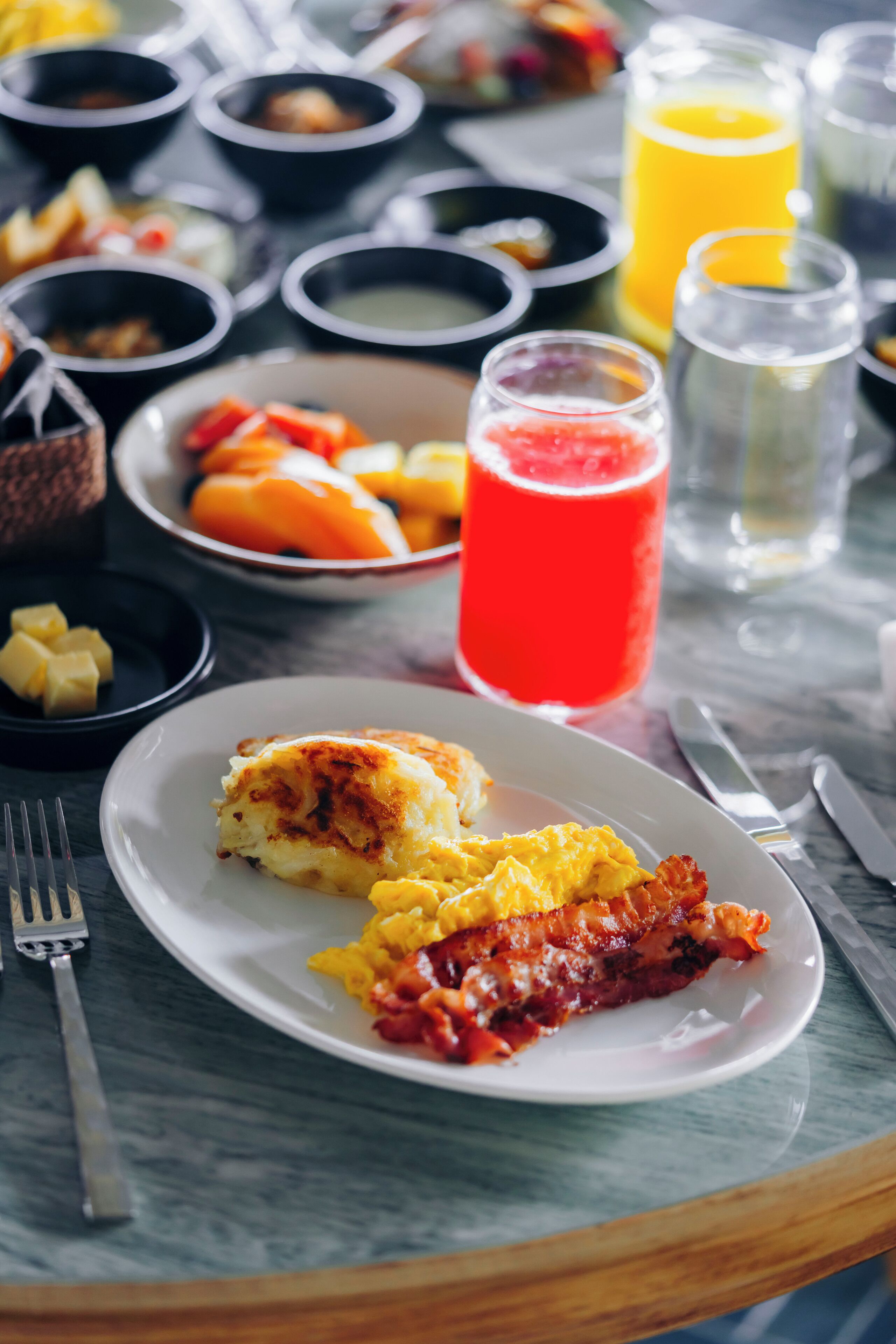 A breakfast setting with a plate of eggs, bacon, and toast, accompanied by various drinks and side dishes.