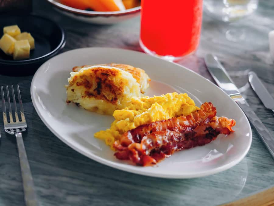A breakfast setting with a plate of eggs, bacon, and toast, accompanied by various drinks and side dishes.