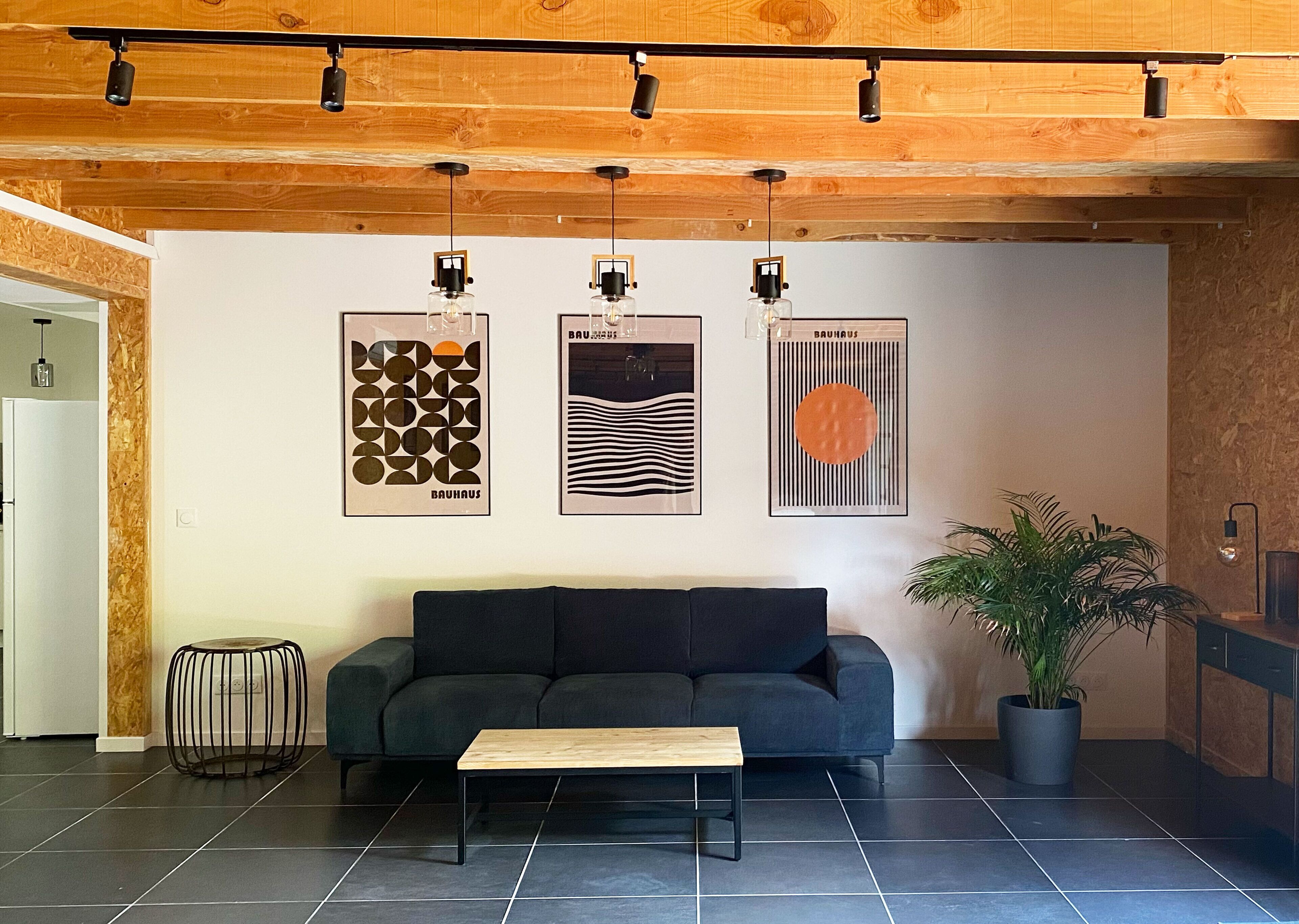 Een moderne woonkamer met een donkergrijze bank, een houten salontafel en een potplant. Drie ingelijste kunstwerken hangen aan de muur.