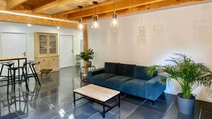 A spacious living area with a dark blue sofa, a wooden dining table, and a coffee table. - Loft Bike & Chill Mont Ventoux – Hot Tub – Secure Bike Storage (Entrechaux)