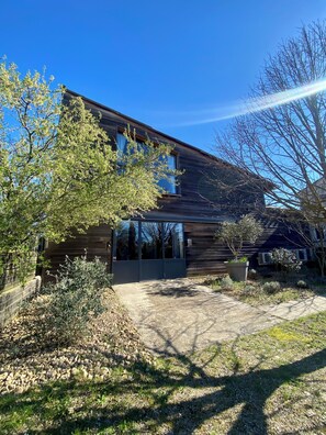 A modern wooden building with a large glass door entrance, surrounded by trees and a gravel path. - Loft Bike & Chill Mont Ventoux – Hot Tub – Secure Bike Storage (Entrechaux)