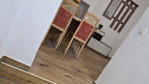 Un escalier en bois mène à une pièce où se trouvent un lit, une table de chevet et une fenêtre avec des stores.