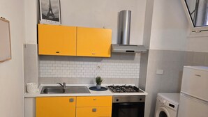 Une cuisine compacte avec des meubles de couleur jaune, une cuisinière en acier inoxydable, un four encastré et un lave-linge.