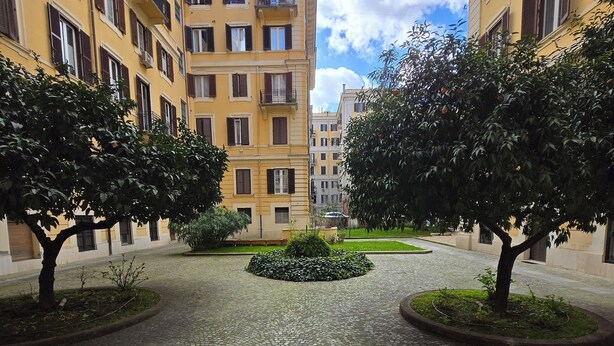 Une cour dallée de pierres, entourée d’immeubles jaunes à plusieurs étages, dotés de balcons et de fenêtres.