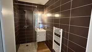 A bathroom with dark tiled walls, a shower, a sink, and a white towel rack.