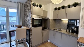 A modern kitchen with a built-in oven, microwave, and sink, a dining area with a table and chairs, and a balcony with a view.