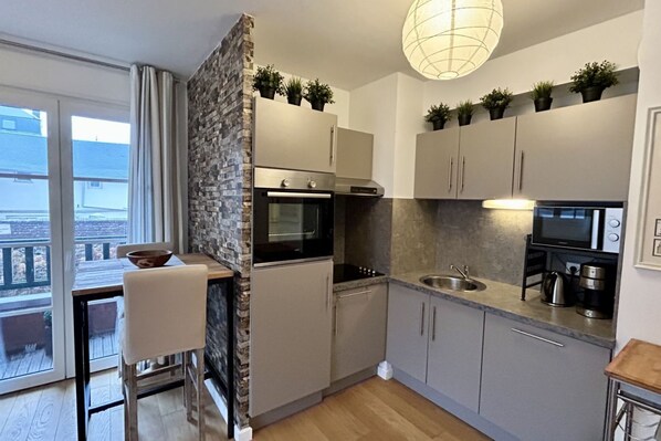 A modern kitchen with a built-in oven, microwave, and sink, a dining area with a table and chairs, and a balcony with a view.