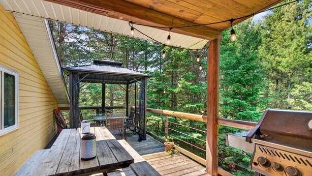 A covered deck with a grill, a table with chairs, and a gazebo.
