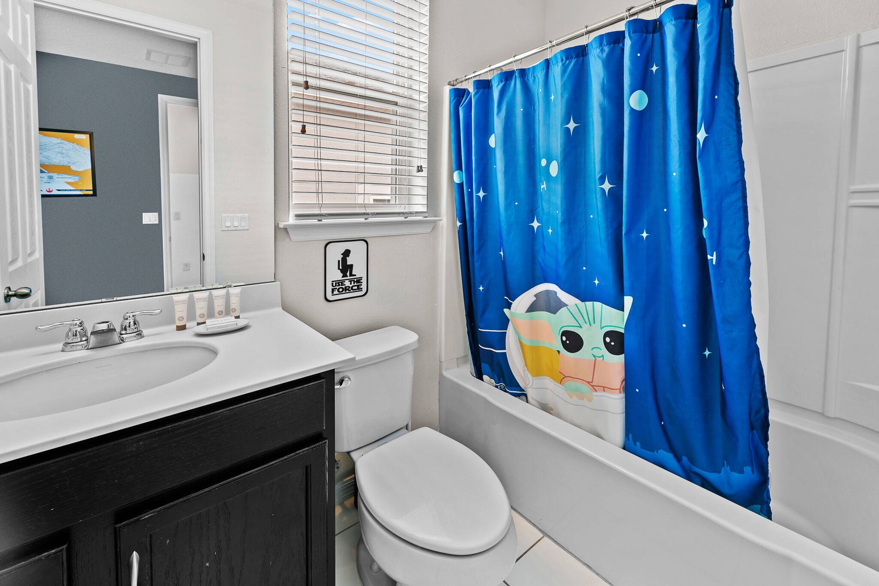Un baño con lavamanos blanco, inodoro y cortina de ducha con un personaje de caricatura.