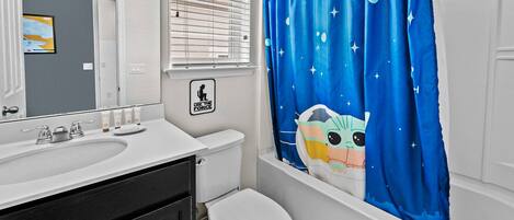Un baño con lavamanos blanco, inodoro y cortina de ducha con un personaje de caricatura.