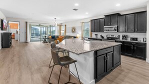 A modern kitchen with granite countertops, dark cabinetry, and a central island with bar stools. - Spacious 7Bd Next to Clubhouse at Solara Resort (Kissimmee)