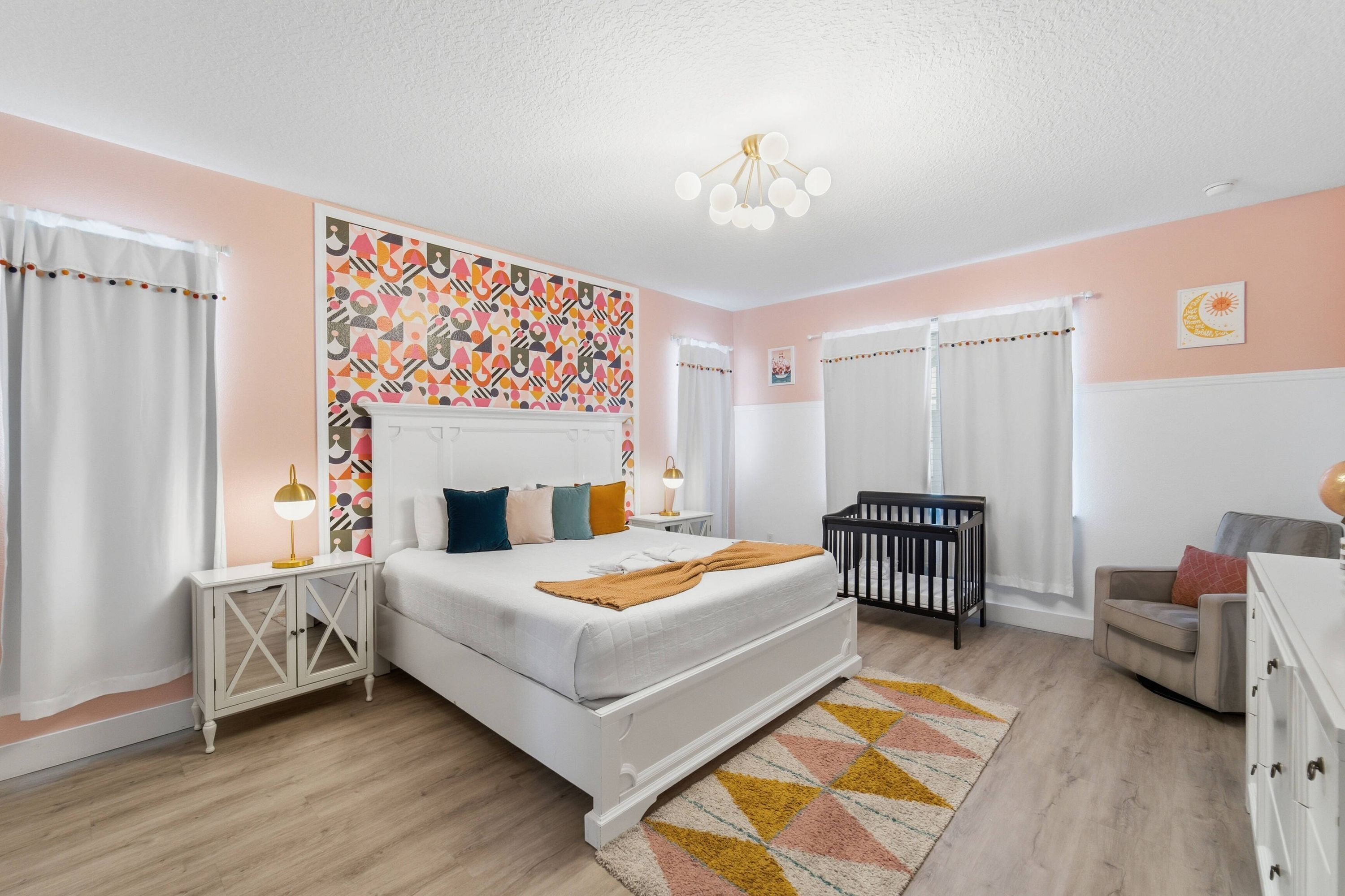 A bedroom with a bed, bedside tables, a crib, and a wall with a geometric pattern.