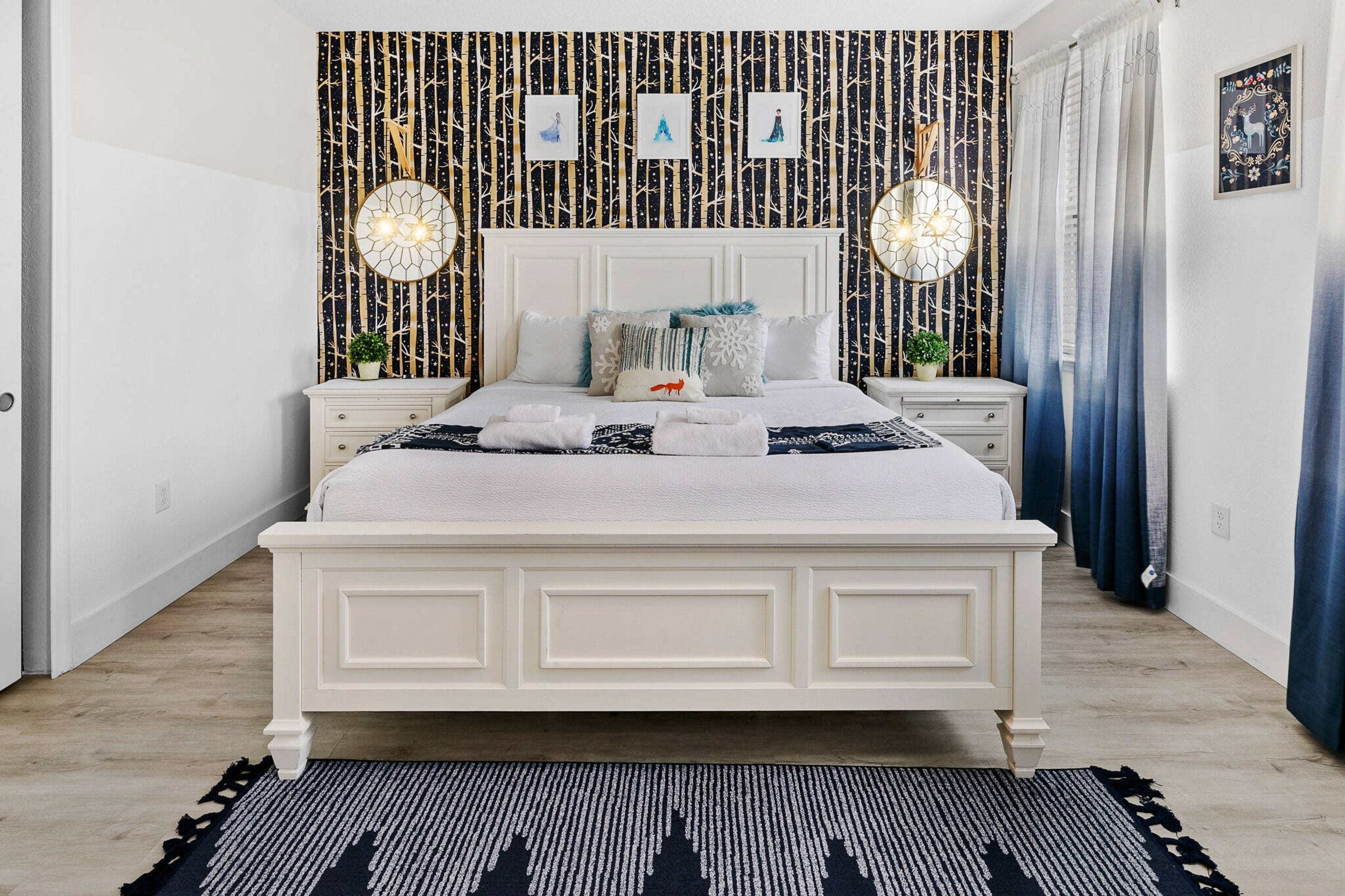 Un dormitorio ordenado con una cama grande, mesitas de noche y un papel tapiz estampado.
