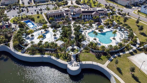 An aerial view of a resort with a central pool, a bridge, and surrounding greenery. - Spacious 7Bd Next to Clubhouse at Solara Resort (Kissimmee)