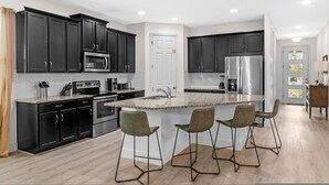 A modern kitchen with dark cabinets, stainless steel appliances, and a central island with bar stools. - Spacious 7Bd Next to Clubhouse at Solara Resort (Kissimmee)