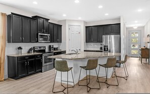 A modern kitchen with dark cabinets, stainless steel appliances, and a central island with bar stools.