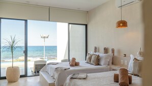 Une chambre d’hôtel avec deux lits, une grande fenêtre donnant sur la plage, une plante en pot et un luminaire suspendu.