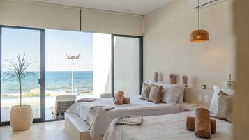 Une chambre d’hôtel avec deux lits, une grande fenêtre donnant sur la plage, une plante en pot et un luminaire suspendu.