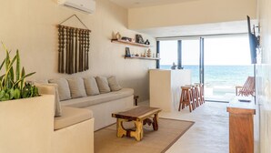 Un salon moderne avec un canapé, une table basse en bois et une vue sur l’océan grâce à de grandes fenêtres.